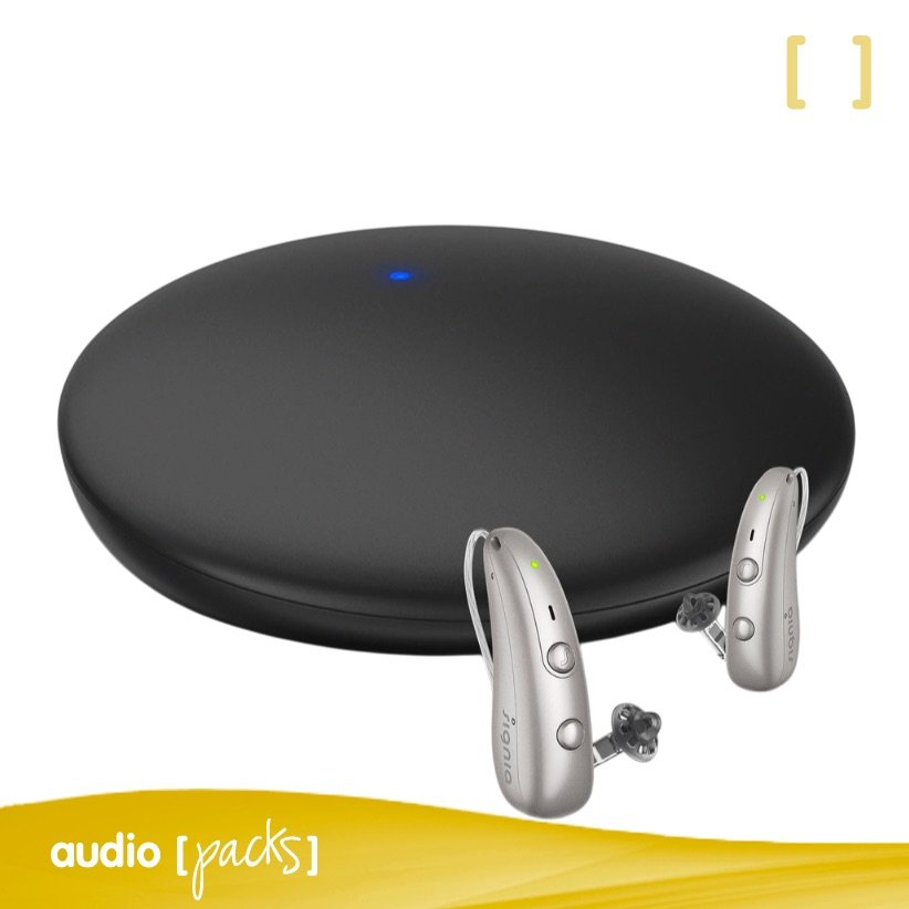 Solucions auditives 13 Dispositiu Signia TV Sound aparellat, amb un LED blau encès, juntament amb un parell d'audiòfons Signia en color plata, llestos per a la transmissió d'àudio.